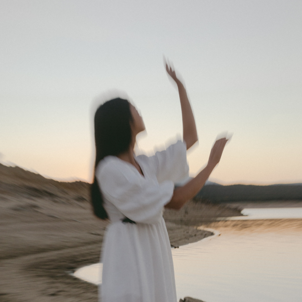 Woman by water in a dress with her arms in the air