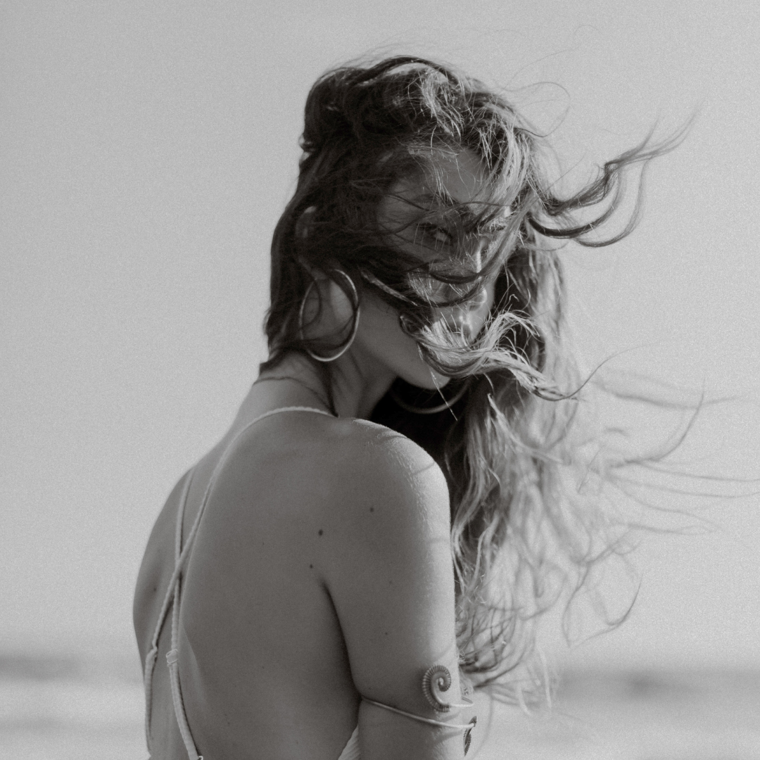 Woman looking back at camera by the ocean with her hair blowing in the wind. Black and white image.